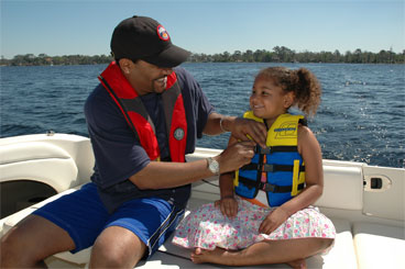 picture of coastie checking personal flotation device on child while sitting on boat